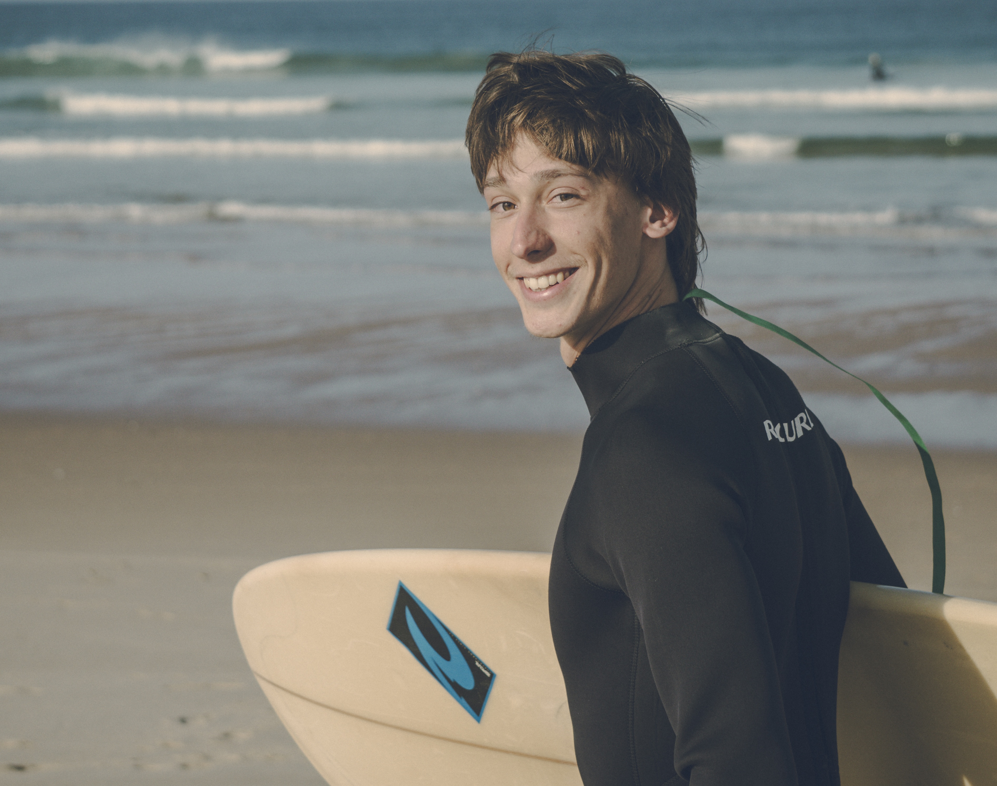 Gründer von NOTIDE am Strand mit Surfbrett lächelnd