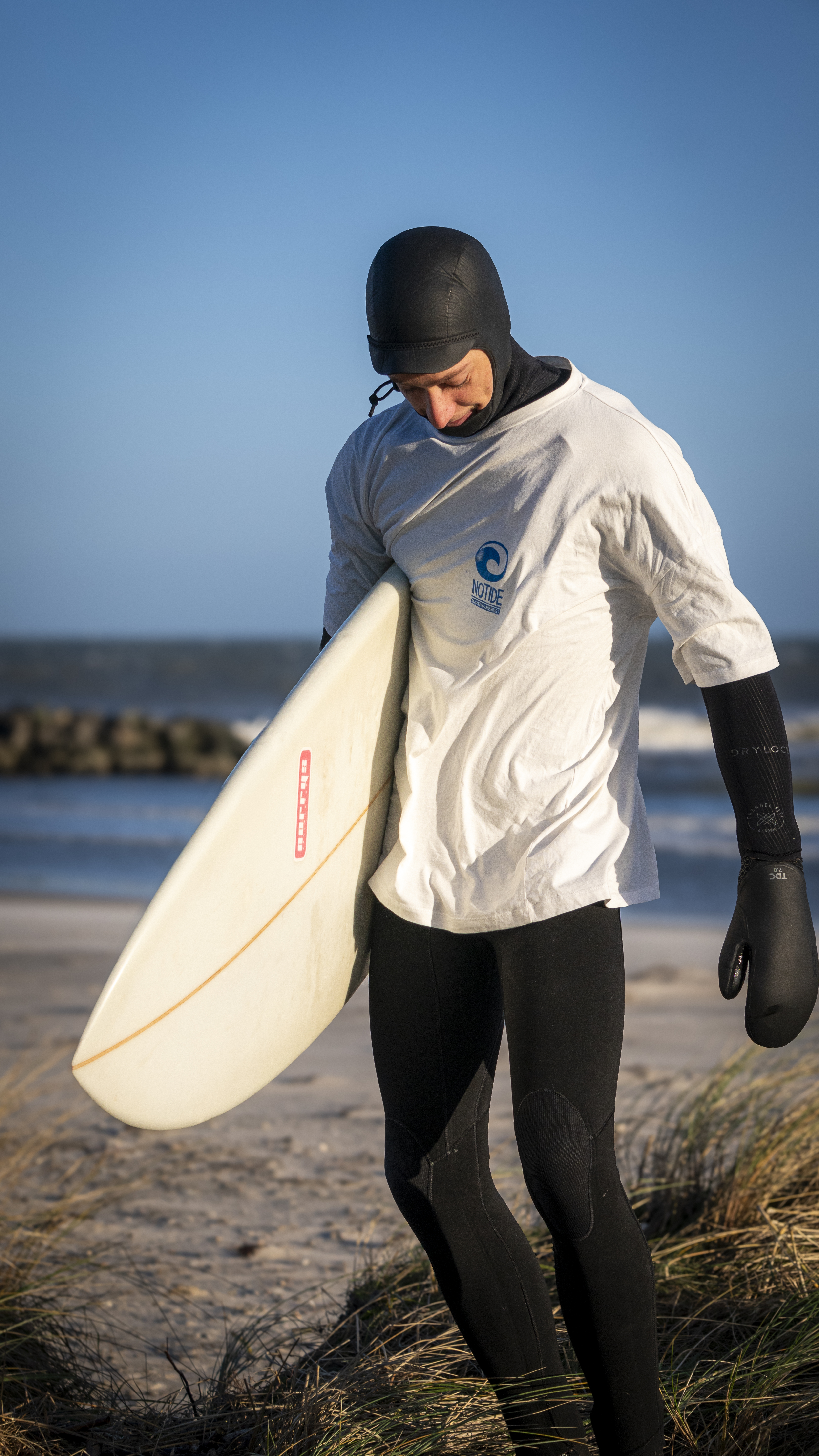surfer mit notide t-shirt über dem neopren anzug am strand mit surfbrett